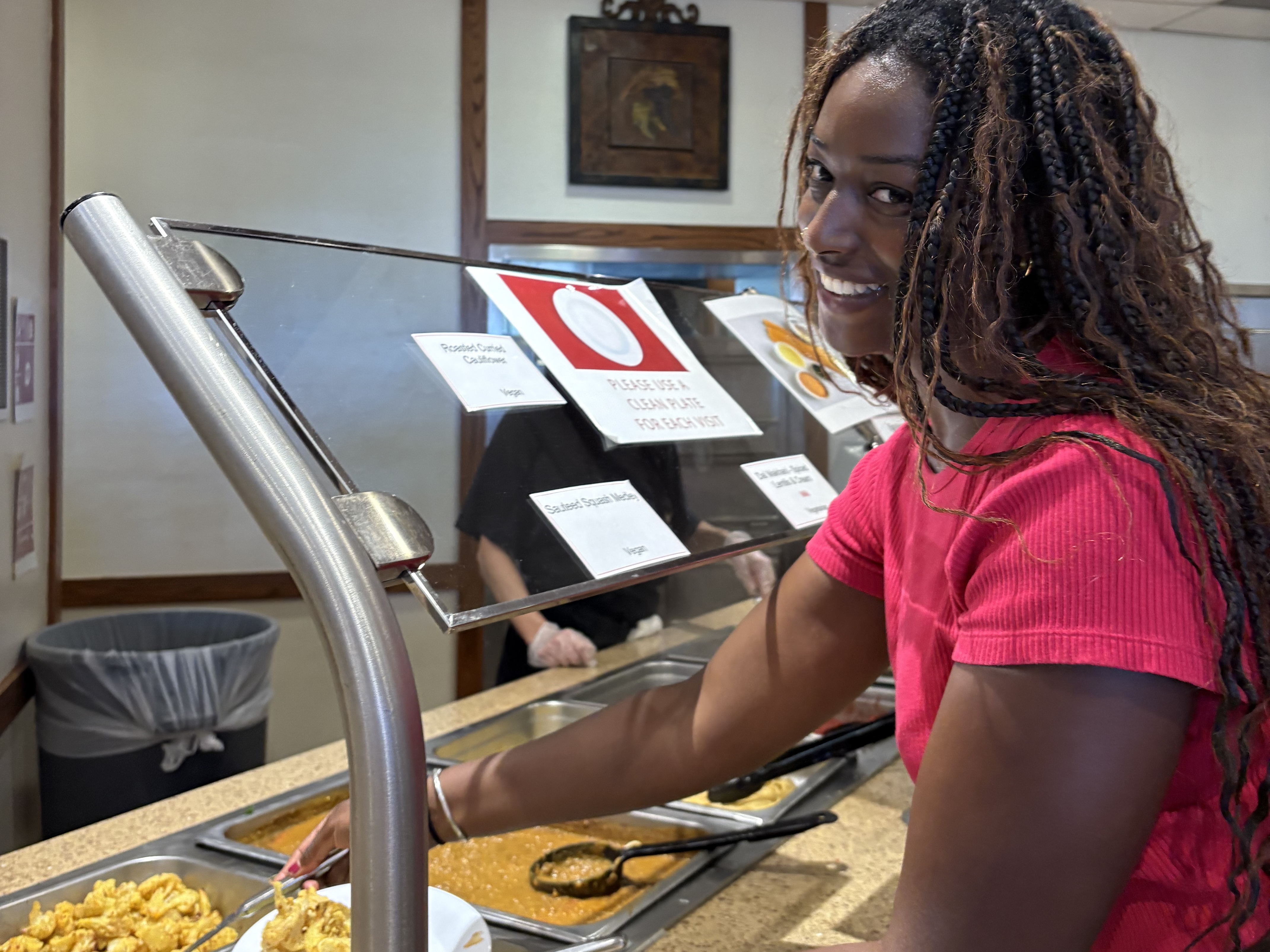 A smiling Black person serves herself food from a buffet