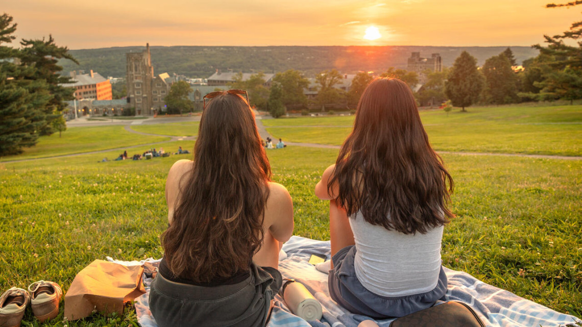 two students sitting on the hill looking at the sunset