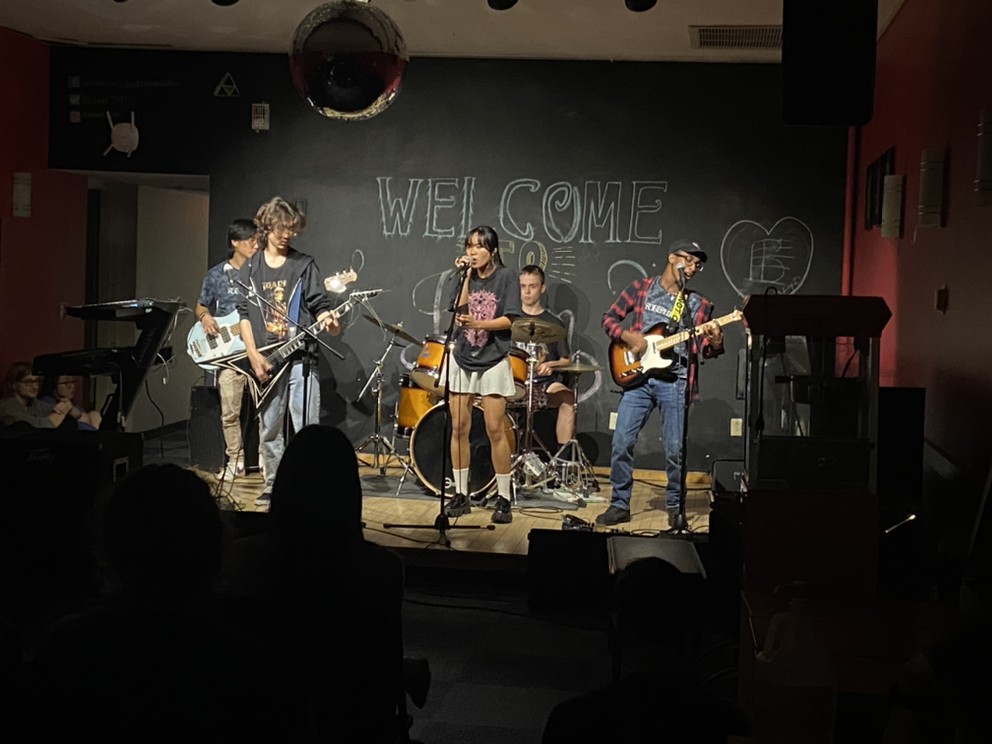 Students perform instruments on stage during an Open Mic night at the JAM program house