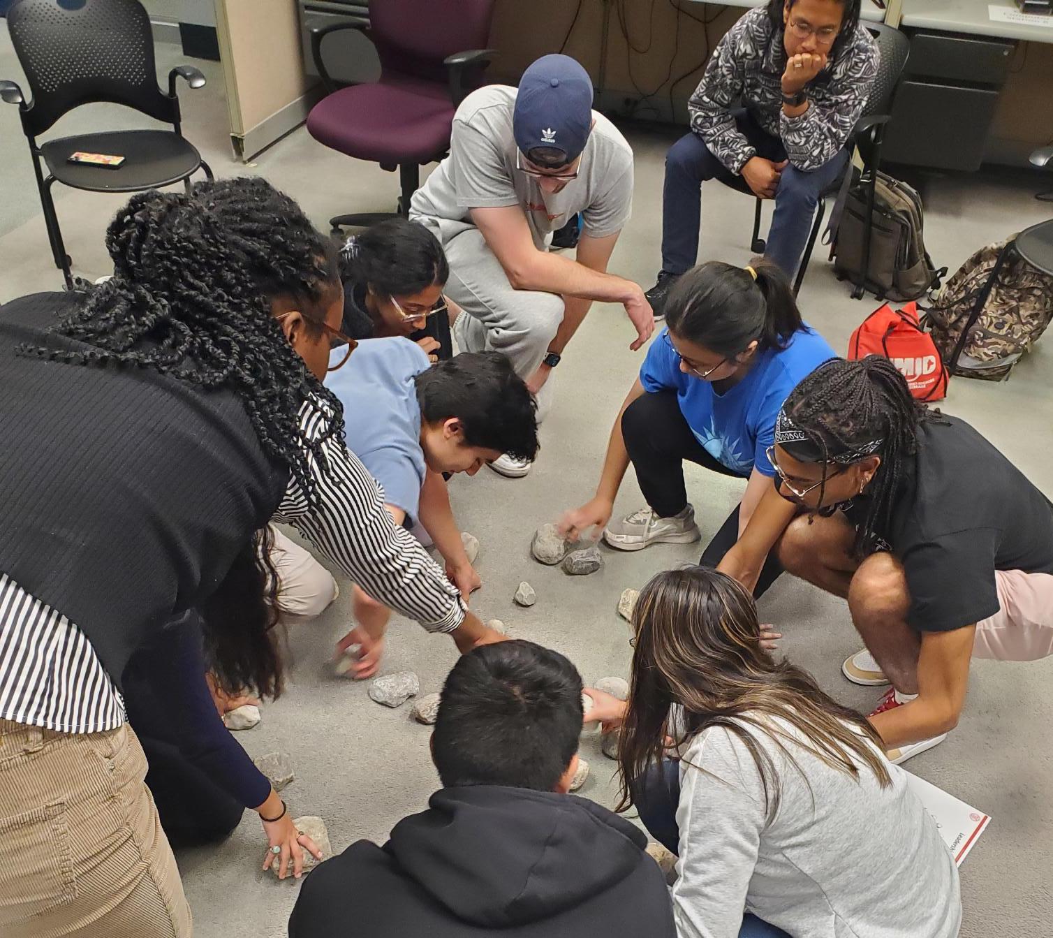 Students gathered around a circle of rocks inside