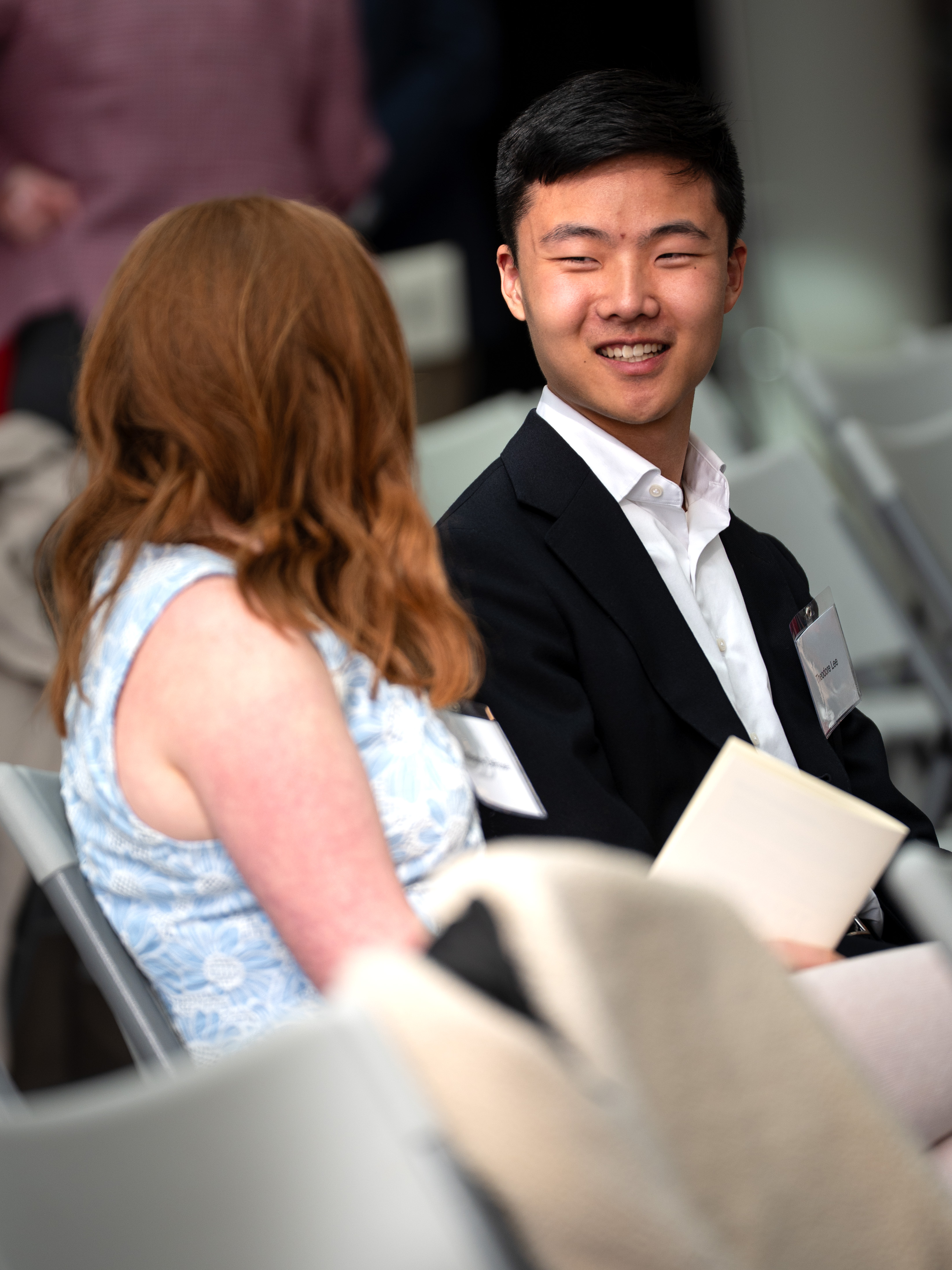 A student in a suit smiles while talking with another student at a Cornell fellowship recognition ceremony.