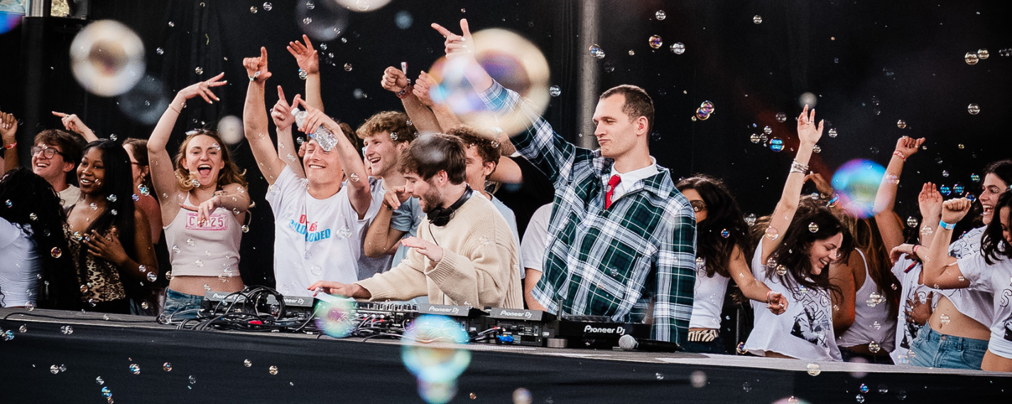 Students dancing and smiling on a stage with a dj and bubbles