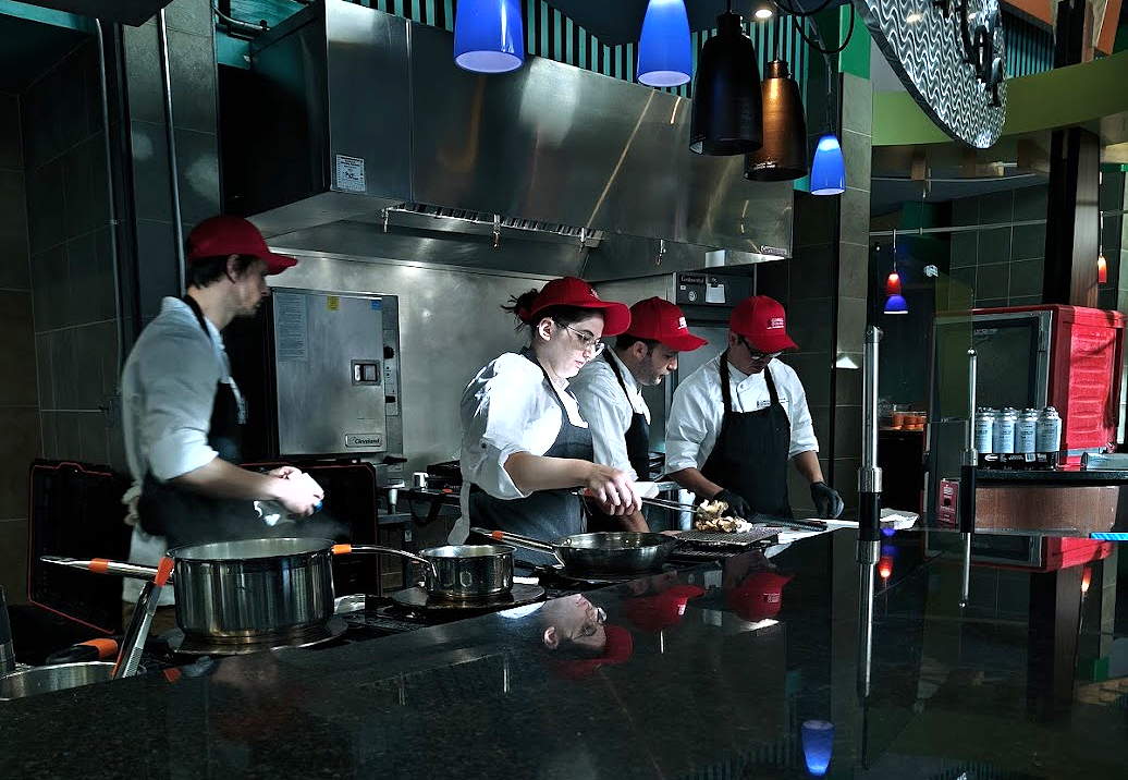 Four chefs wearing red caps cooking in a shared kitchen