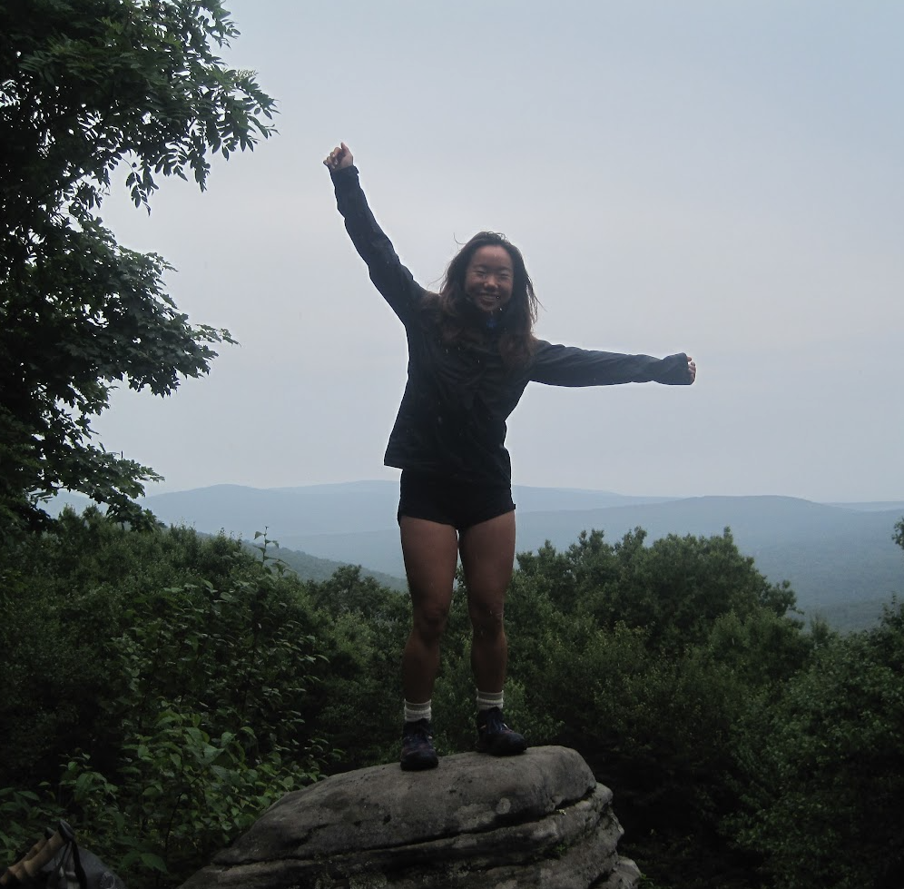 Odyssey trip participant stands on top of a boulder, posing before a great mountainous view.