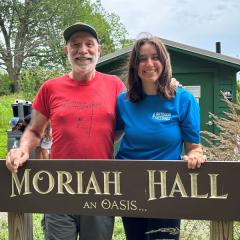 Photo of Bella Threlkeld standng outside in fro of Moriah Hall an Oasis sign