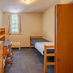 A bedroom in with a twin bed, dresser, table, and chair.