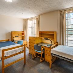 A triple room with three twin beds, desks, chairs, lamps, dressers, and a window.