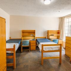 A triple room with three twin beds, desks, chairs, lamps, dressers, and a window.