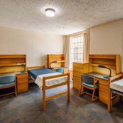 A triple room with three twin beds, desks, chairs, lamps, dressers, and a window.
