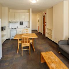 A living room, kitchen, and dining room with tables, chairs, a couch, coffee table, fridge, stove, oven, sink, cabinets, and counters.