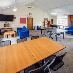 A large lounge in JAM with chairs, tables, couches, a ping pong table, and a TV.
