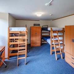 A bedroom with three twin beds, dressers, desks, and chairs