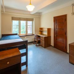 single room with a bed, desk and chair, a nightstand, drawers, and a window.
