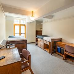 Double room with two beds, two desks and chairs, two nightstands, two sets of drawers, and a window.