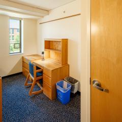 Single room with a bed, desk and chair, drawers, and a window.