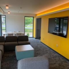 A lounge in Hu Shih Hall with yellow walls, couches, small tables, and a TV hanging on a wall