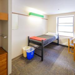 A bedroom in with a twin bed, dresser, table, and chair.