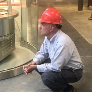 A person wearing a hard hat crouches on a bare concrete floor in an unfinished building