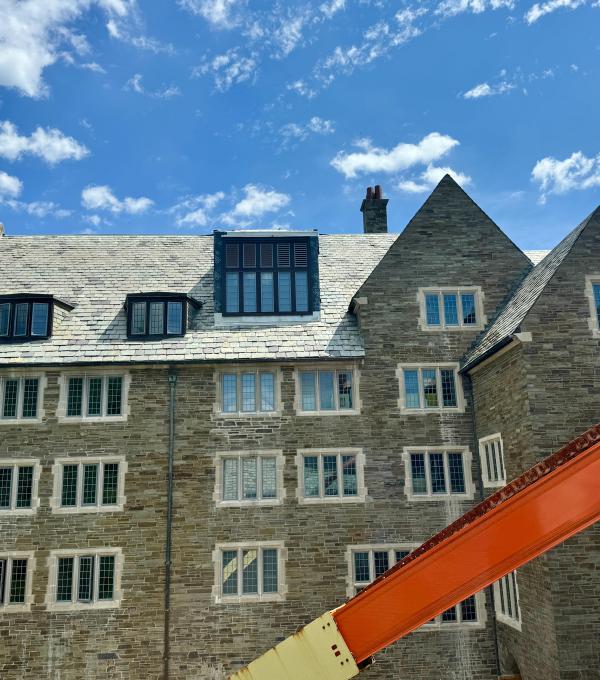 An old-fashioned stone college building with slate tiled roof, and a crane arm extending across the view