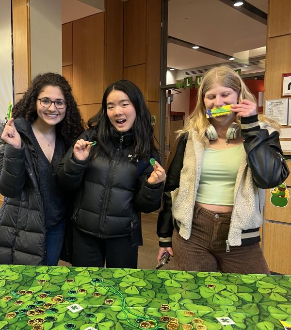 Three students behind a table decorated in green