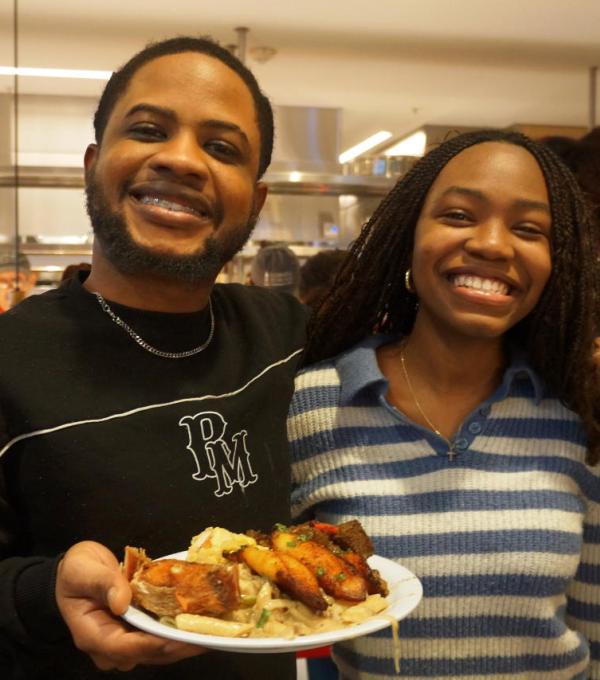 Two Black people smiling, with one holding a plate of food