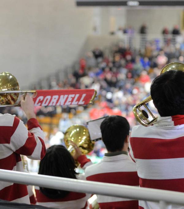 Several band members seen from behind, wearing red and white stripes, with fans in the stands in the background