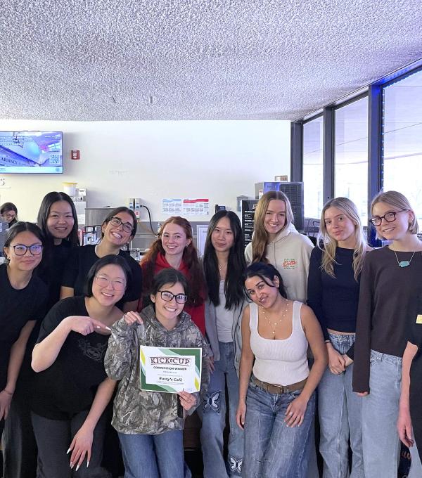 About a dozen people stand in two rows, with one holding a certificate that says Kick the Cup
