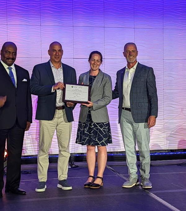 Four people stand on a stage, with one holding up an award