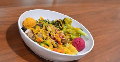 A bowl of food including vegetables and grains on a wooden counter