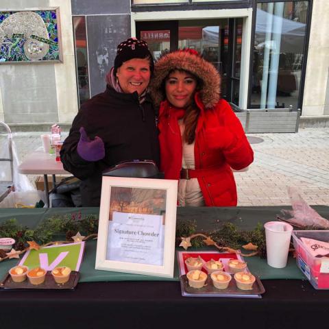 Two people bundled up in warm coats at a chowder event booth