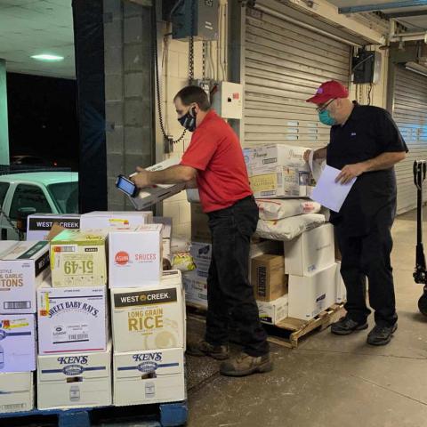 Two people unload a pallet of food supplies at a loading dock
