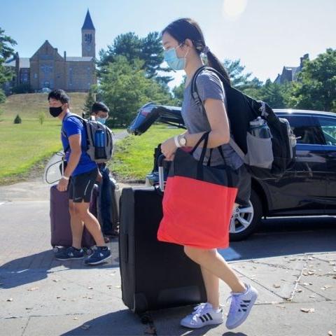 Two students arriving with luggage, with car in the background and the Cornell clocktower in far distance.