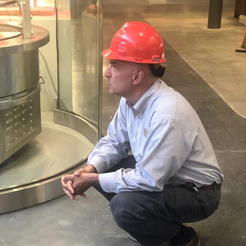 A person wearing a hard hat crouches on a bare concrete floor in an unfinished building