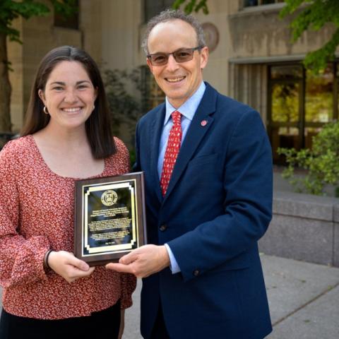 Two people hold plaque and smile at camera