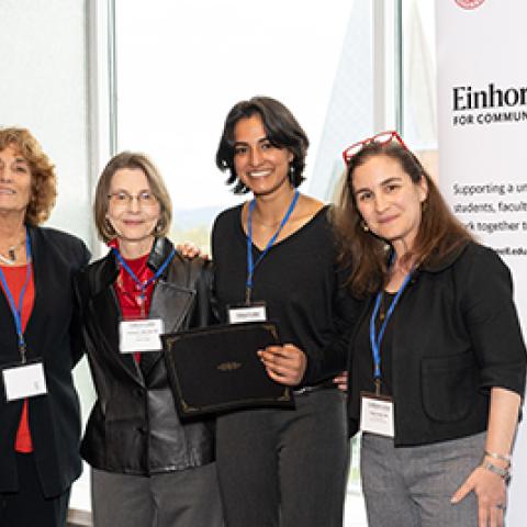 Group of four stands in front of Einhorn Center banner, smiling at camera