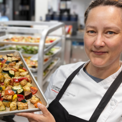 A person in an apron holds up a sheet pan with vegetable chunks