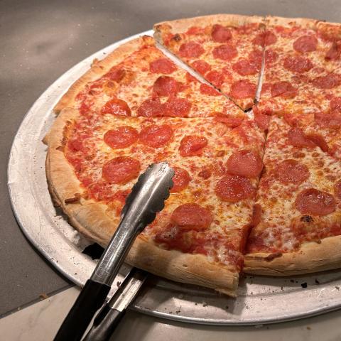 Tongs reach for a slice of pizza out of a pepperoni pizza resting on a pan