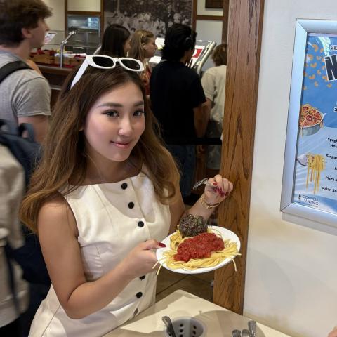 A person holds a plate of spaghetti and sauce