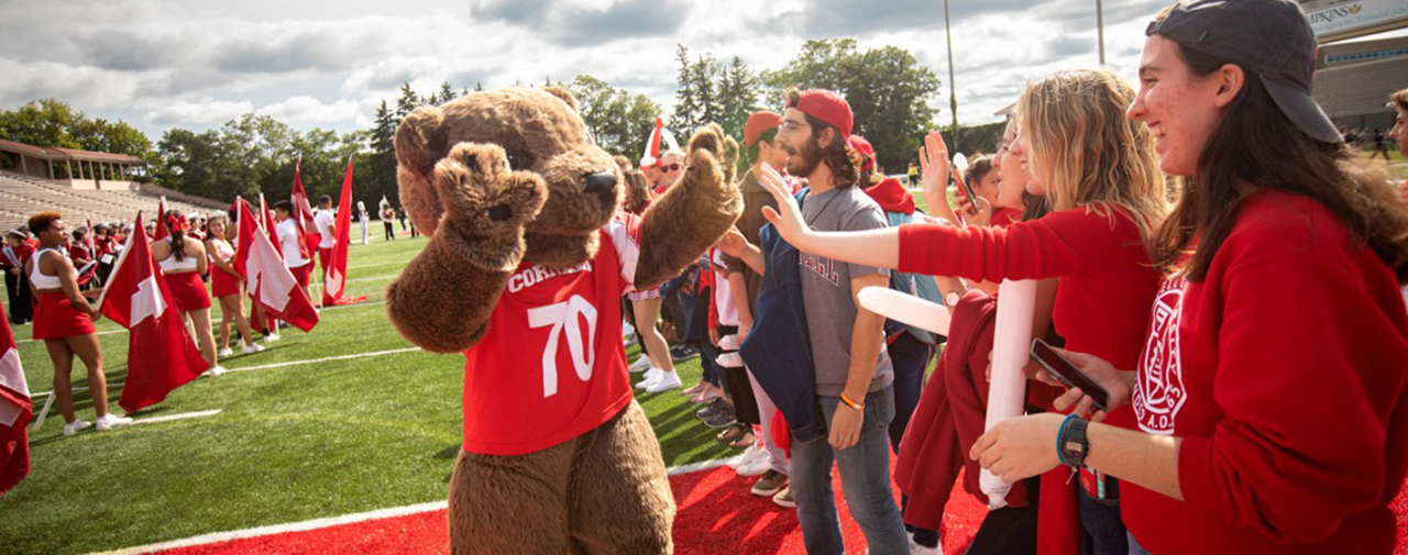 Students high five Touchdown mascot at Homecoming parade on football field