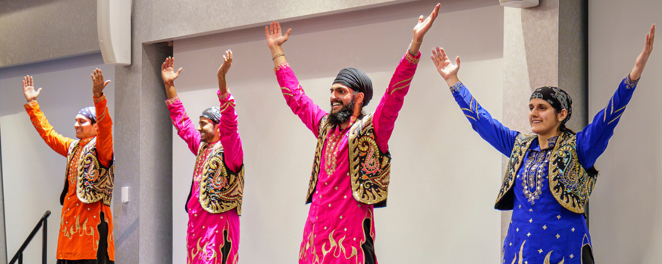 Four dancers pose in Asian outfits on a stage.