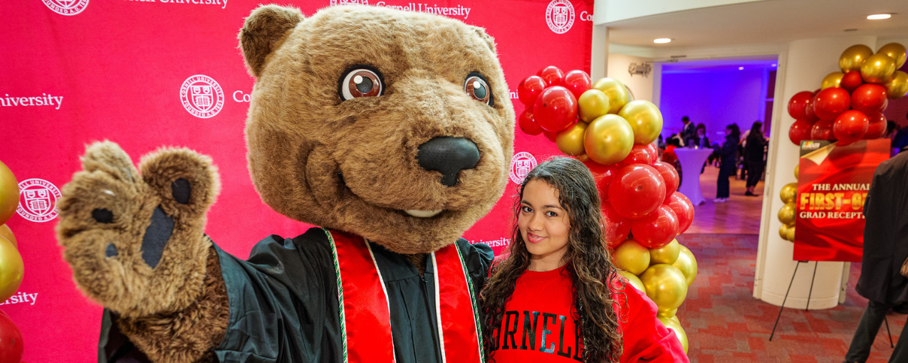 Young woman poses with a bear mascot, against a red background