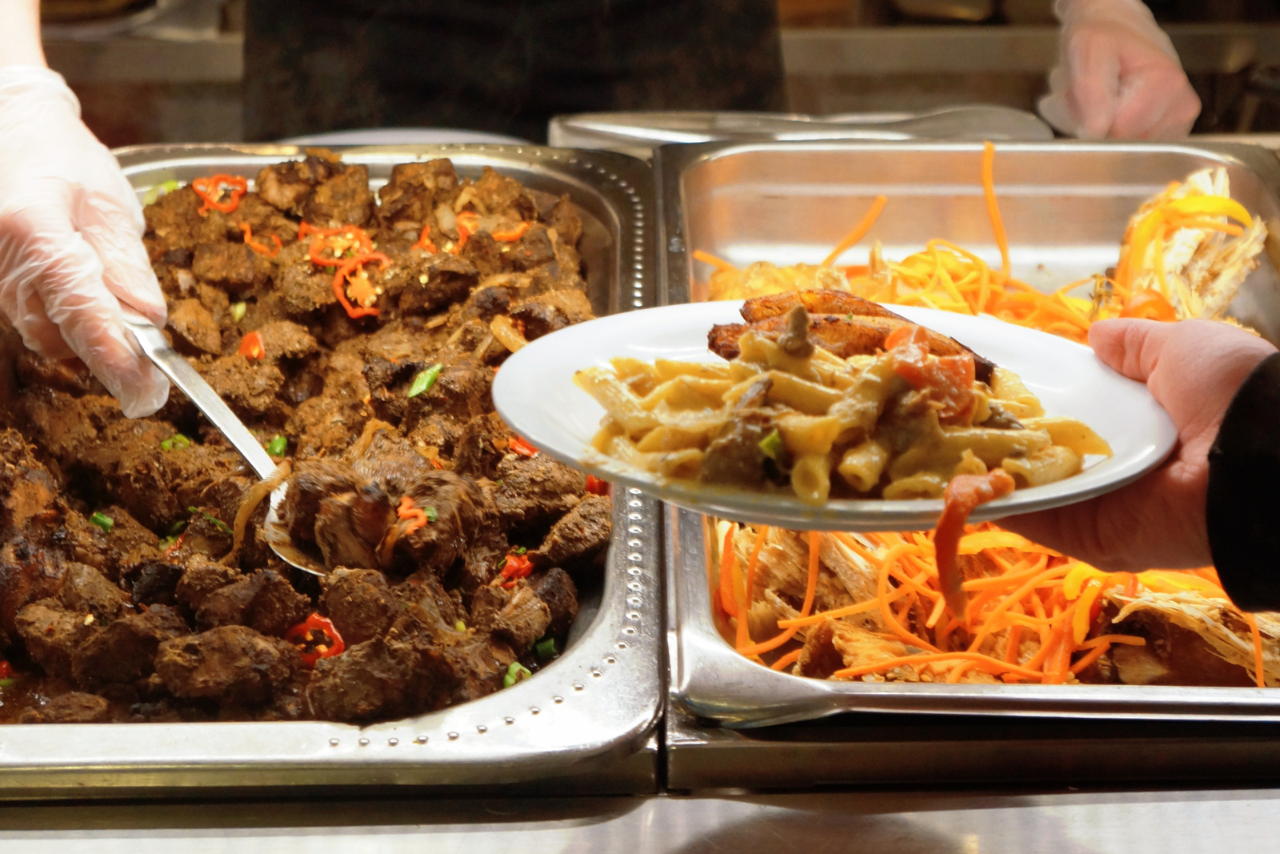 Serving trays of food, with a hand serving food onto a plate