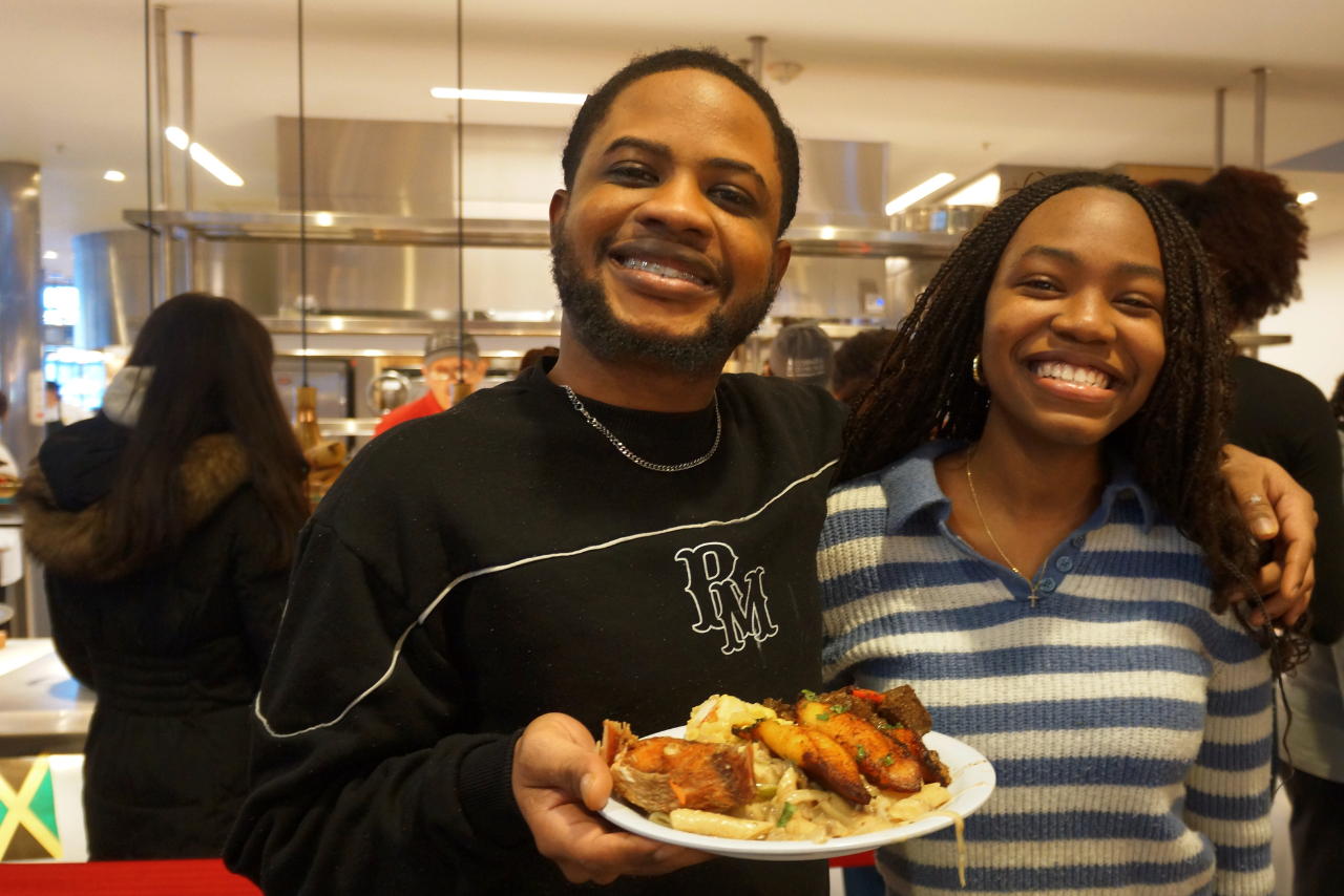 Two Black people smile while one is holding a plate of food