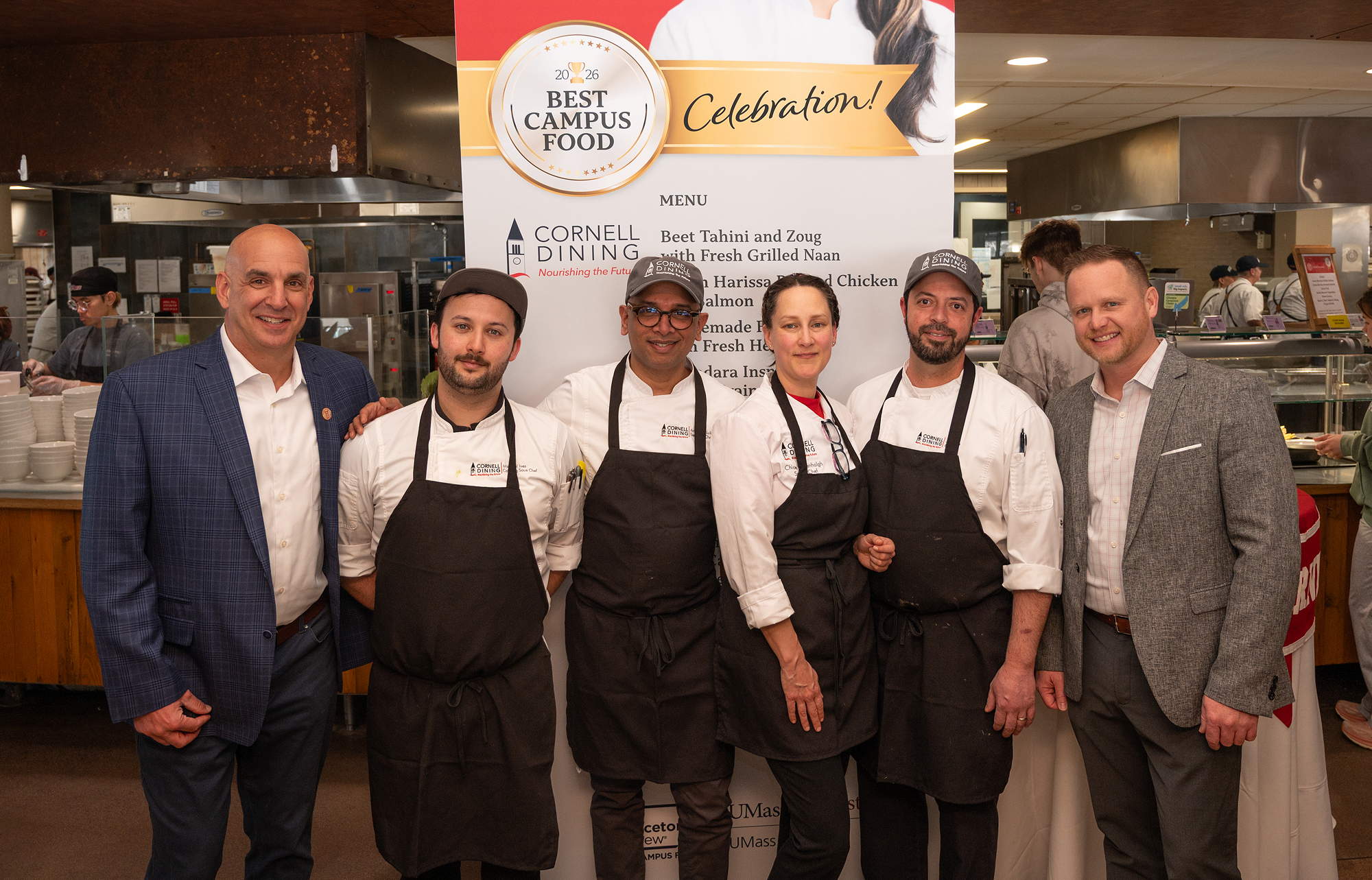 A row of people, four of them in chef coats and aprons, stand in front of a poster