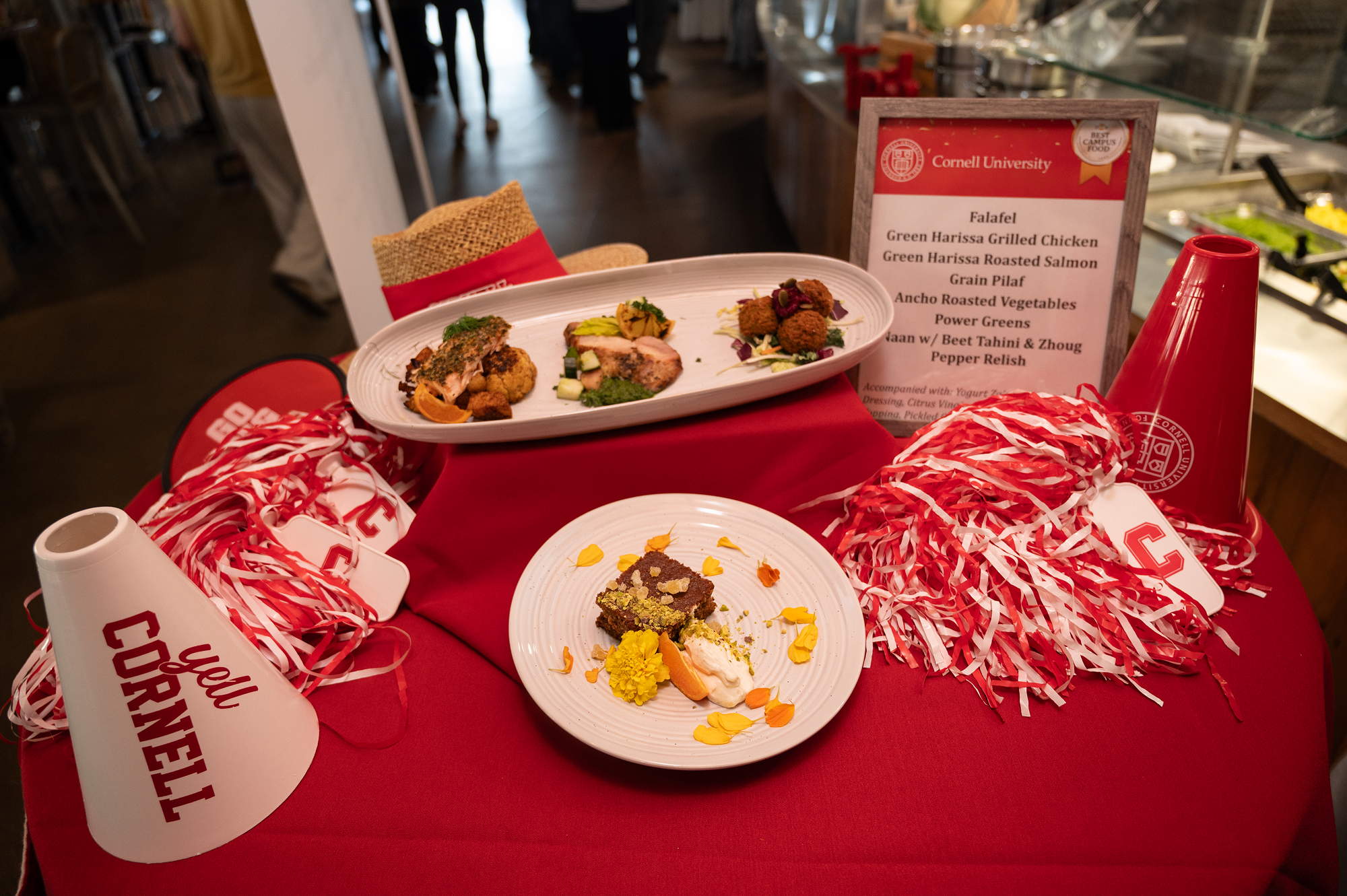 Plates of food on a table with red tablecloth and red and white Cornell fan items such as pom-poms and bullhorns