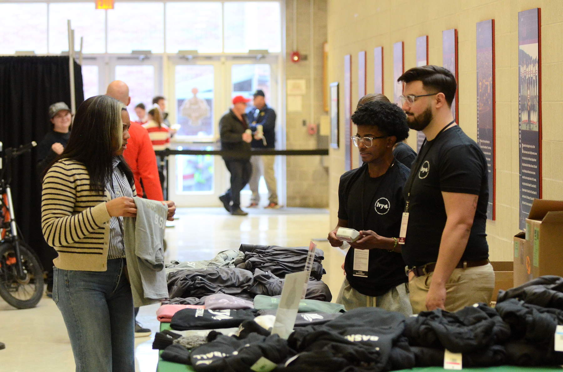 A person holds a shirt in front of a souvenir table with students staffing it behind the table