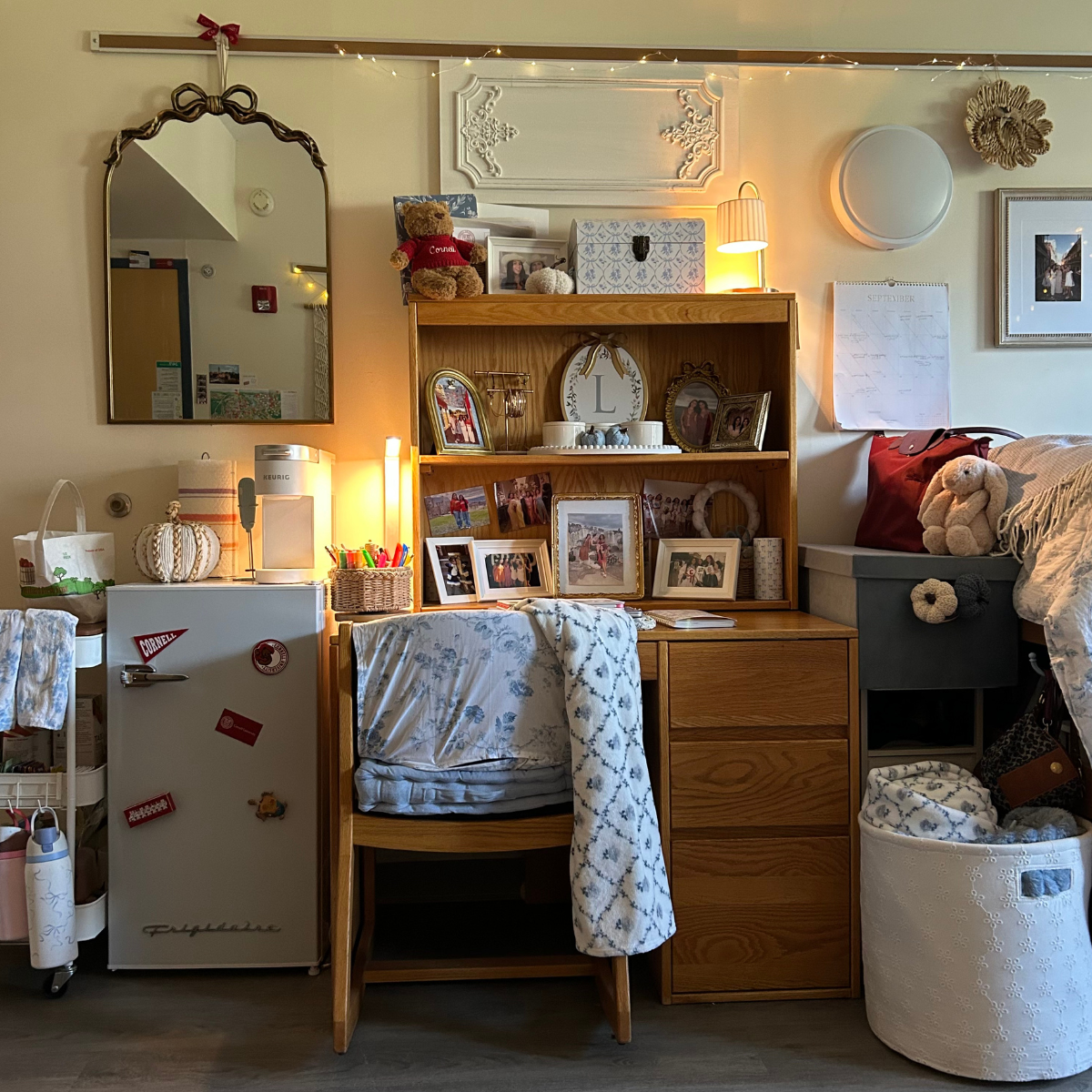 A fully decorated residence hall room study area featuring an oak wood desk with a hutch, a small Frigidaire mini-fridge, and a large decorative mirror.