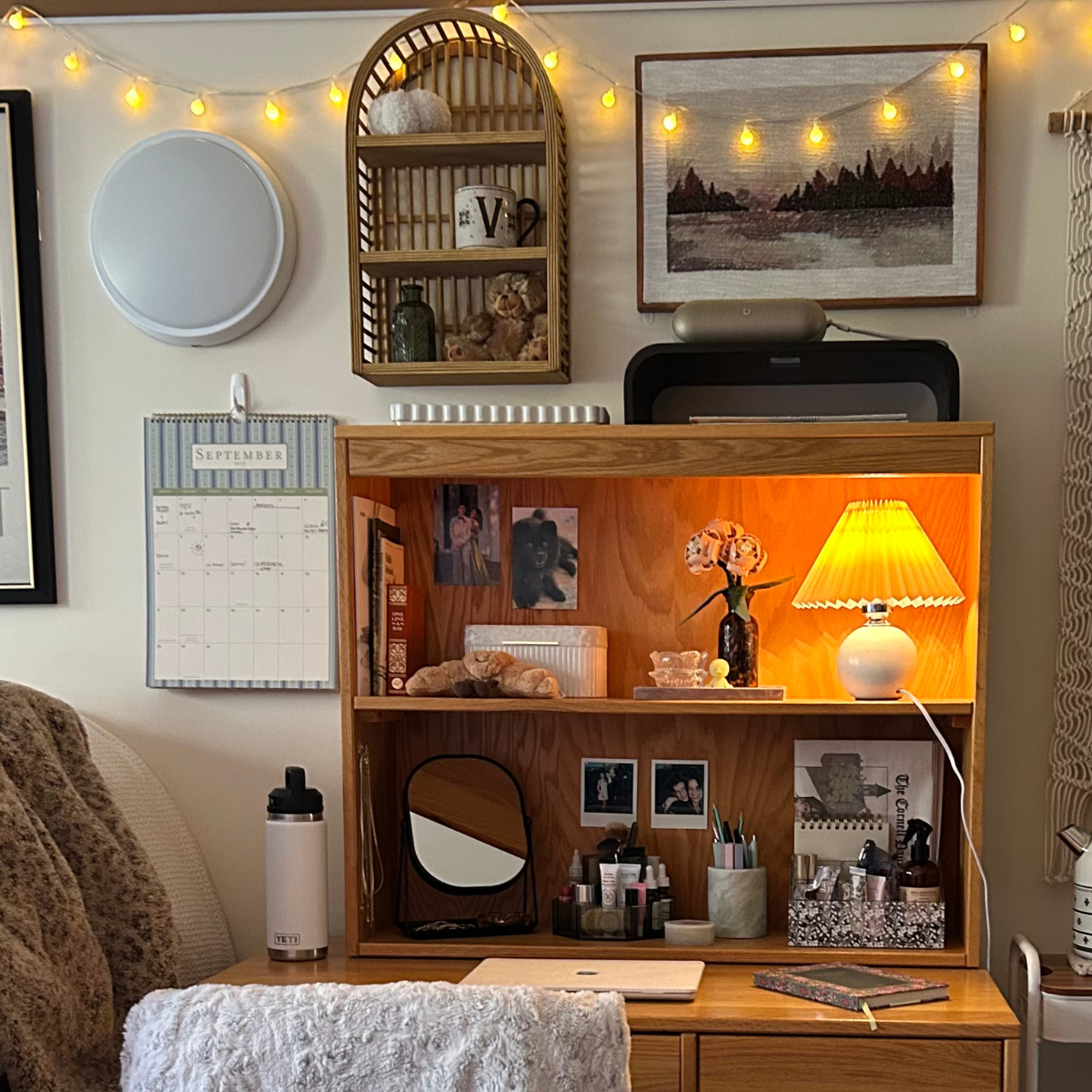 An organized wooden desk and hutch decorated with warm lighting, string lights, framed art, and a variety of study and decorative items