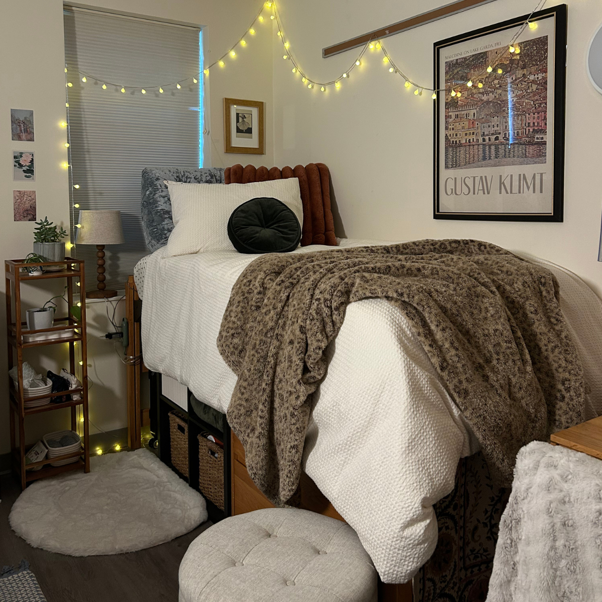 A cozy, decorated residence hall room bed with white bedding, a brown leopard-print throw blanket, and warm yellow string lights overhead