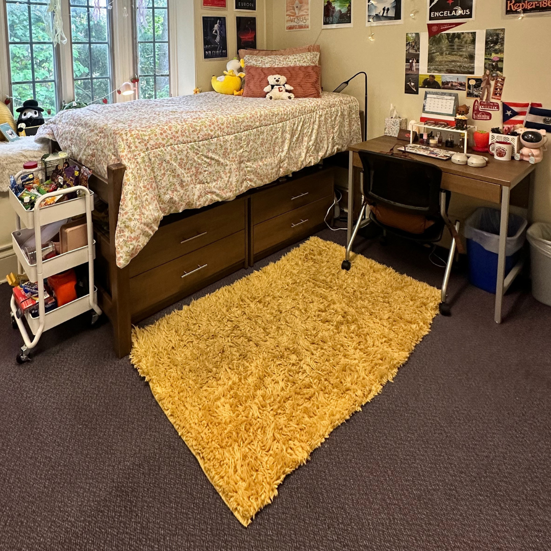 Bed with floral linens, yellow rug, desk with chair